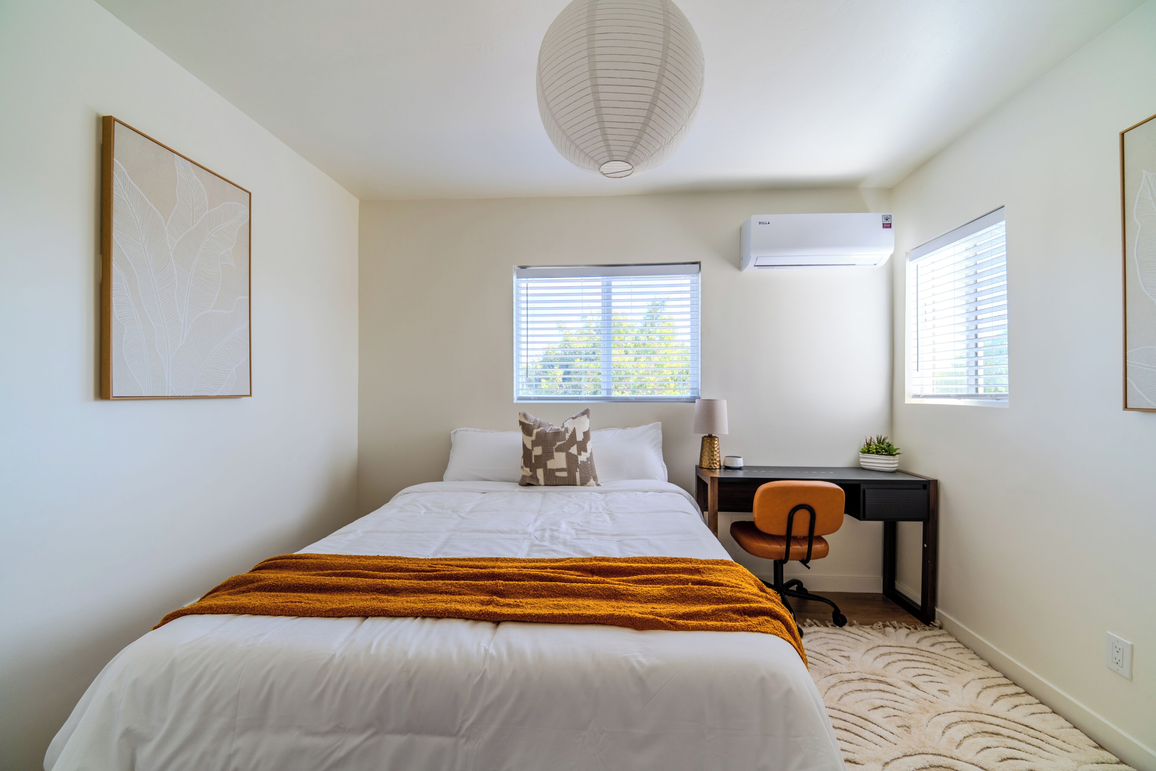 A bedroom with a bed, a desk, a chair, and two windows with blinds.