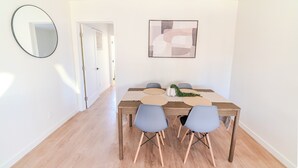 Zona pranzo con tavolo in legno, quattro sedie, uno specchio e un quadro astratto appeso al muro.