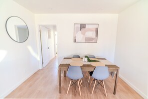 A dining area with a wooden table, four chairs, a mirror, and a wall-mounted abstract painting. - Long Beach 3 Bedroom Apartment Near Beach, Dining, CSULB, Long Beach Airport (Long Beach)