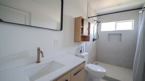 Un bagno con lavandino bianco, un water, una doccia e uno specchio.