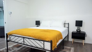 A bedroom with a bed, two bedside tables, a wall-mounted TV, and a door.