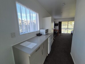 A compact kitchenette with a microwave, a small table, and a chair. - Magnolia Court Motel (Ōpōtiki)