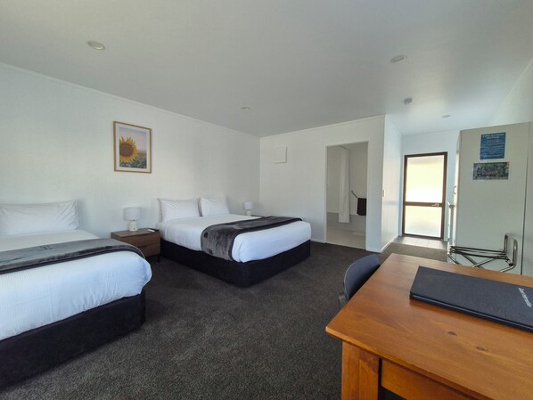 A hotel room with two beds, a desk, a chair, a wardrobe, and a door leading to a bathroom.