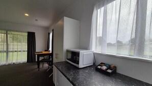 A compact kitchen with a microwave, a small table, and a window with curtains. - Magnolia Court Motel (Ōpōtiki)