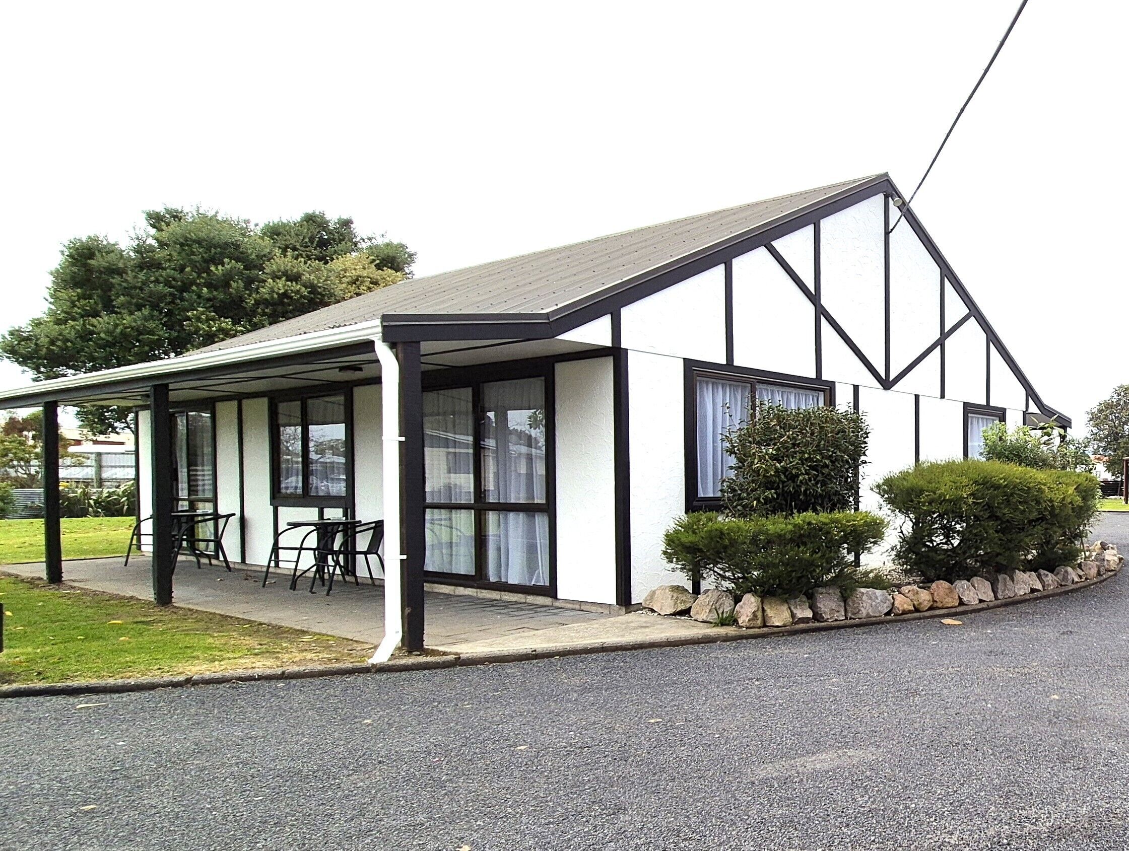 A building with a covered patio area, a pitched roof, and a stone border.