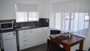 A compact kitchen with a microwave, sink, and a dining area with a table and chairs. - Magnolia Court Motel (Ōpōtiki)