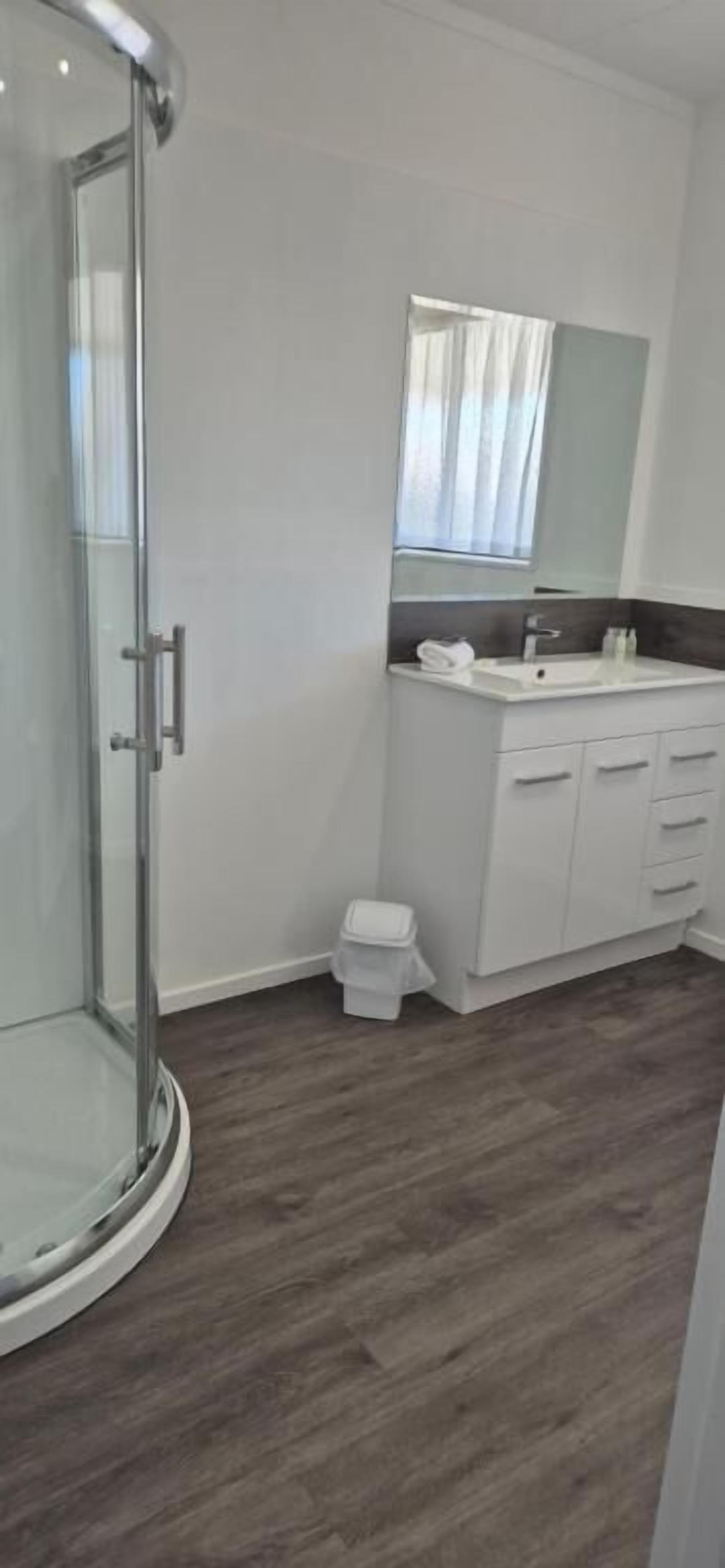 A modern bathroom with a glass shower enclosure, a white vanity with a mirror, and a small trash bin.