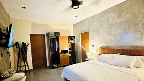 Une chambre à coucher comprenant un lit, un ventilateur de plafond, une armoire, un téléviseur et un petit tabouret.