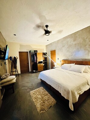 A bedroom with a bed, a ceiling fan, a wardrobe, a TV, and a small stool.