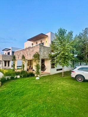 A modern two-story house with a stone facade, a covered patio, and a white car parked in the driveway.