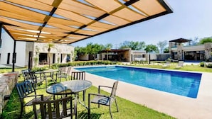 Une piscine avec un patio couvert, des sièges extérieurs et un bâtiment moderne en arrière-plan.