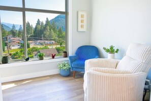 Ein Zimmer mit großem Fenster, blauem Stuhl, weißem Stuhl und mehreren Blumentöpfen.