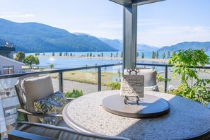 Ein Balkon mit Seeblick und Bergblick, ein runder Tisch mit einem Schild und zwei Stühle mit Kissen.