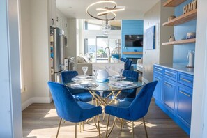 Eine moderne Küche mit blauen Schränken, eine Essecke mit blauen Stühlen und einem Glastisch, sowie ein im Schrank integriertes Fernsehgerät über der Arbeitsfläche.