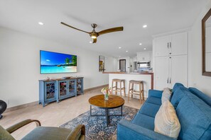A modern living room with a blue sofa, a round coffee table, and a TV displaying a beach scene.