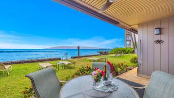 An outdoor patio with a table set for two, overlooking a beach with a clear view of the ocean and a distant island.