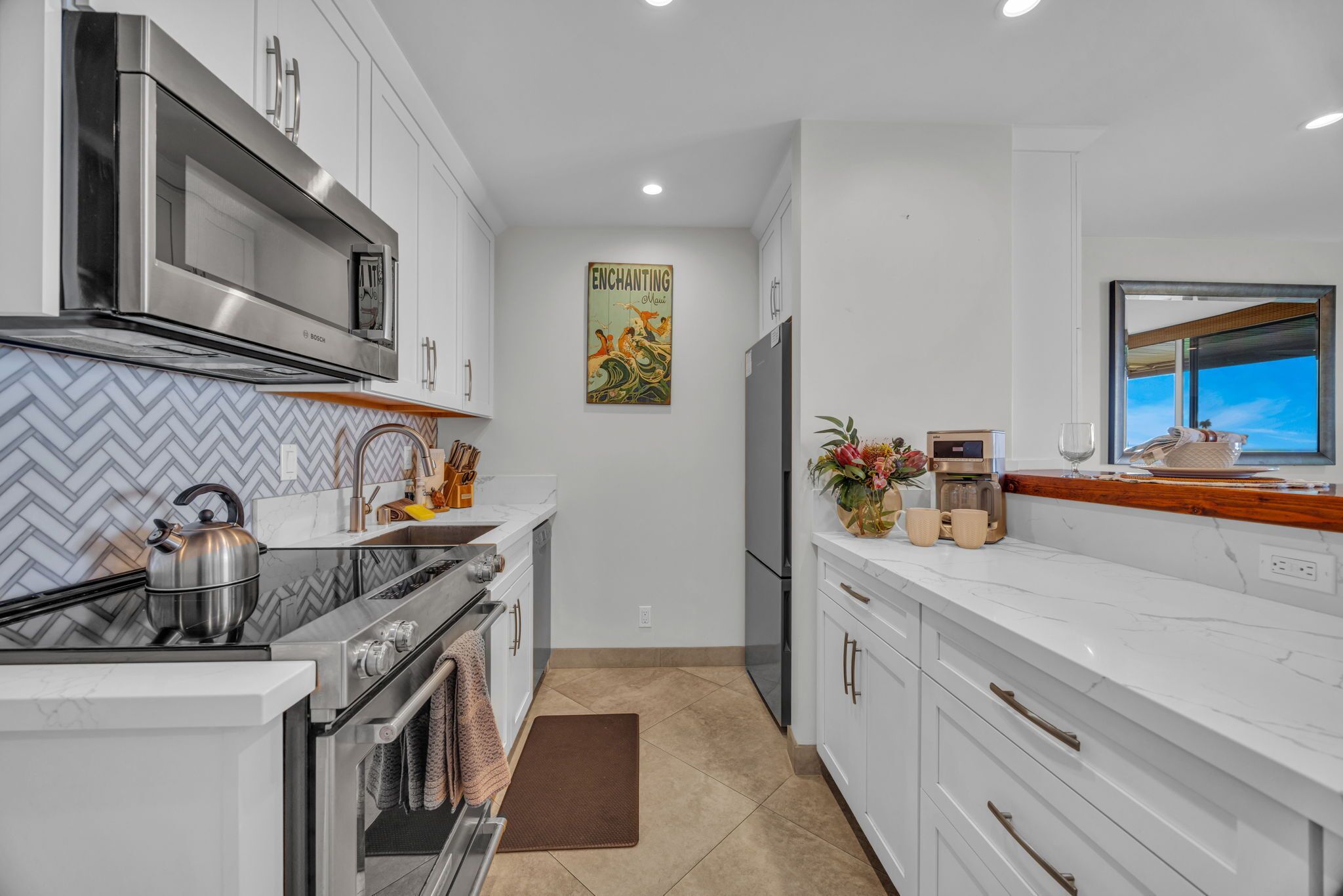 A modern kitchen with white cabinetry, stainless steel appliances, and a herringbone tile backsplash.