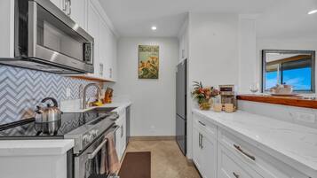 A modern kitchen with white cabinetry, stainless steel appliances, and a herringbone tile backsplash.