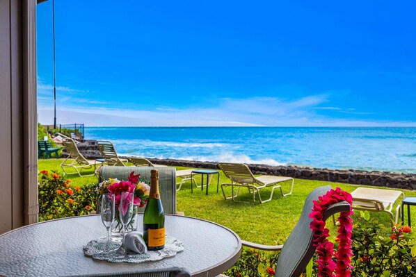A table with a bottle of champagne, glasses, and a decorative item, overlooking a beach with lounge chairs and a clear view of the ocean.