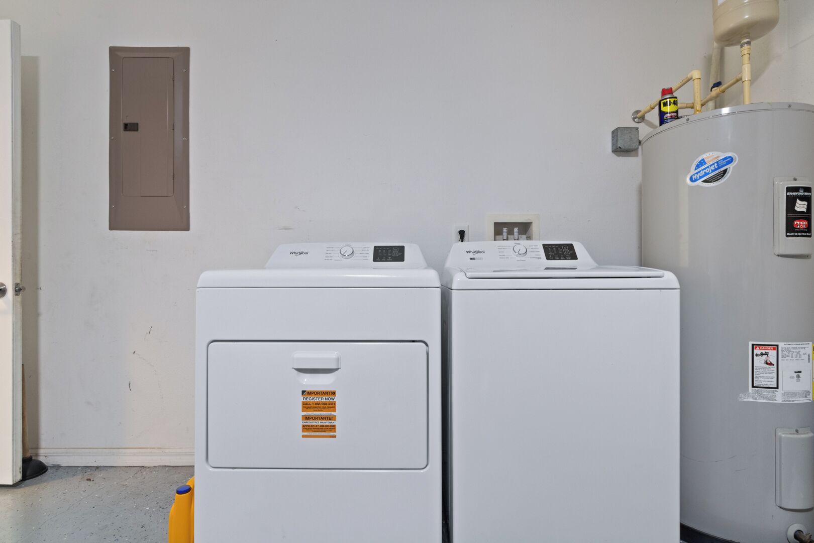 Two white Whirlpool washers and a large water heater in a utility room.