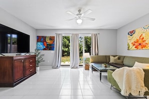 A modern living room with a flat-screen TV, a sofa, a coffee table, and a ceiling fan. - Family-Friendly 3BR Townhouse with Outdoor Patio & Fire Pit 🌴 (Cape Canaveral)
