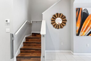 A staircase with wooden steps and white handrails, a wall-mounted mirror, and a painting on the wall. - Family-Friendly 3BR Townhouse with Outdoor Patio & Fire Pit 🌴 (Cape Canaveral)