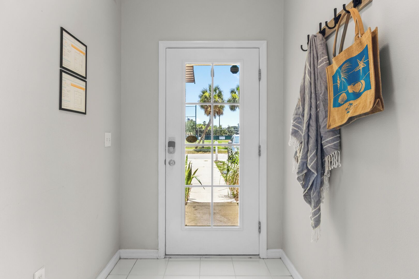 A hallway with a white door, a view of palm trees and a parking lot, and a wall with a towel rack and a framed certificate.