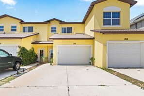 A residential building with two garages, a driveway, and a parked vehicle. - Family-Friendly 3BR Townhouse with Outdoor Patio & Fire Pit 🌴 (Cape Canaveral)