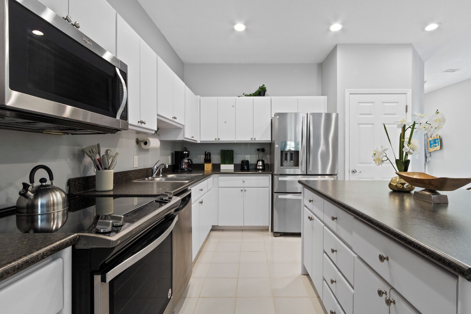 Una cocina moderna con electrodomésticos de acero inoxidable, armarios blancos y piso de baldosas.
