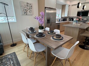 Eine moderne Küche mit einem Edelstahl-Kühlschrank, einem Esstisch mit weißen Stühlen und einer Vase mit violetten Blumen.