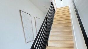 Uma escadaria com degraus de madeira e corrimãos pretos, que dá acesso a um andar superior.