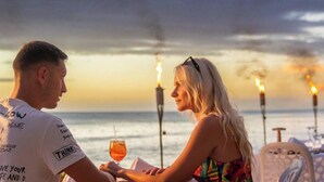 Una pareja sentada a una mesa con vista al mar y un atardecer de fondo.