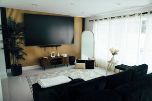 Un salon moderne avec un téléviseur à écran plat, un grand miroir, une plante en pot et un canapé de couleur foncée.
