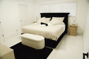 A bedroom with a bed, a bedside table, a nightstand, a door, and a window. - Skylux Ocean House: 3BR Private Pool, Game Room & Cinema-Size TV (Hollywood)
