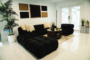 A modern living room with a black sofa, a round coffee table, and a large potted plant. - Skylux Ocean House: 3BR Private Pool, Game Room & Cinema-Size TV (Hollywood)