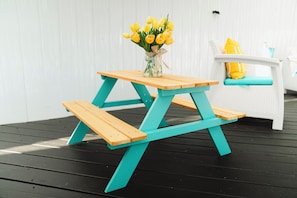 A picnic table with a vase of yellow flowers on top, a white chair with a yellow cushion, and a small yellow bag on the chair. - Skylux Ocean House: 3BR Private Pool, Game Room & Cinema-Size TV (Hollywood)