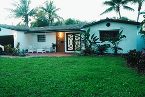 A two-story house with a tiled roof, a front porch with white chairs, and a small garden area. - Skylux Ocean House: 3BR Private Pool, Game Room & Cinema-Size TV (Hollywood)