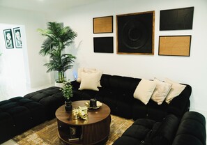 A living room with a black sofa, a round coffee table, and a potted plant. - Skylux Ocean House: 3BR Private Pool, Game Room & Cinema-Size TV (Hollywood)