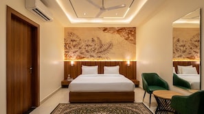 A hotel room with a large bed, a wooden headboard, a green chair, a small table, and a ceiling fan.