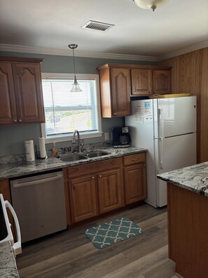 A kitchen with wooden cabinets, a white refrigerator, a coffee maker, and a window with blinds. - Oceanfront 4BR, 2BA Holden Beach retreat (Holden Beach)