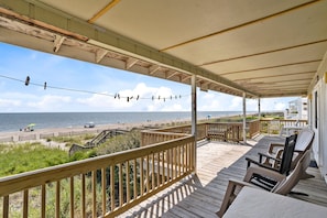 A wooden deck with a view of the beach, a covered area with chairs, and a fence. - Oceanfront 4BR, 2BA Holden Beach retreat (Holden Beach)