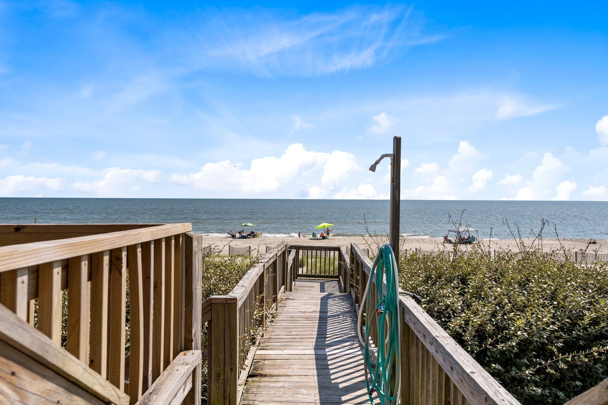 A wooden boardwalk leading to a beach with umbrellas and people.