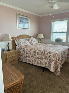 A bedroom with a bed, bedside tables, a lamp, a chair, a window with blinds, and a ceiling fan. - Oceanfront 4BR, 2BA Holden Beach retreat (Holden Beach)