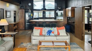 Een moderne keuken met een centraal eiland, een zithoek met een bank en stoelen, en een groot raam met uitzicht.