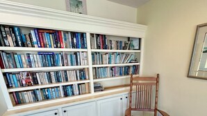 Ein Zimmer mit einer großen Bücherwand, einem Holzbstuhl und einem gerahmten Bild an der Wand.