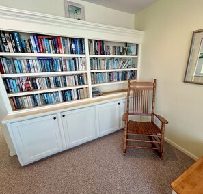 Ein Zimmer mit einer großen Bücherwand, einem Holzbstuhl und einem gerahmten Bild an der Wand.