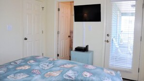 Ein Schlafzimmer mit einem Bett, einem an der Wand befestigten Fernseher, einer Tür und einem Fenster mit Jalousien.
