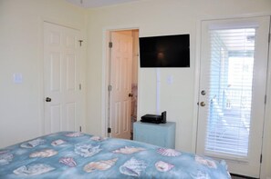Ein Schlafzimmer mit einem Bett, einem an der Wand befestigten Fernseher, einer Tür und einem Fenster mit Jalousien.