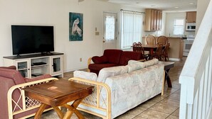 Een woonkamer met een televisie, bank en een eethoek met stoelen.