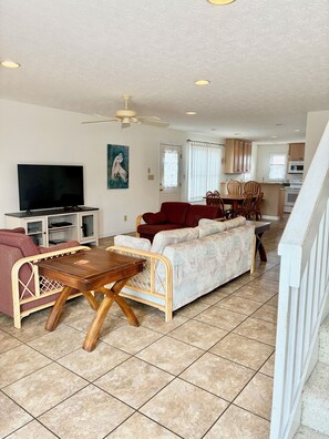 A living room with a television, sofa, and dining area with chairs. - 4BR, 4.5BA  Holden Beach home (Holden Beach)